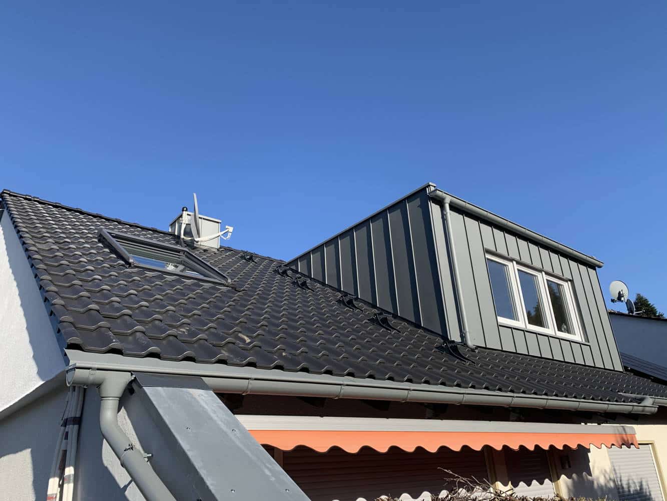 Sehr schönes neues Dach mit einem zinkverkleideten Ausbau vor blauem Himmel.