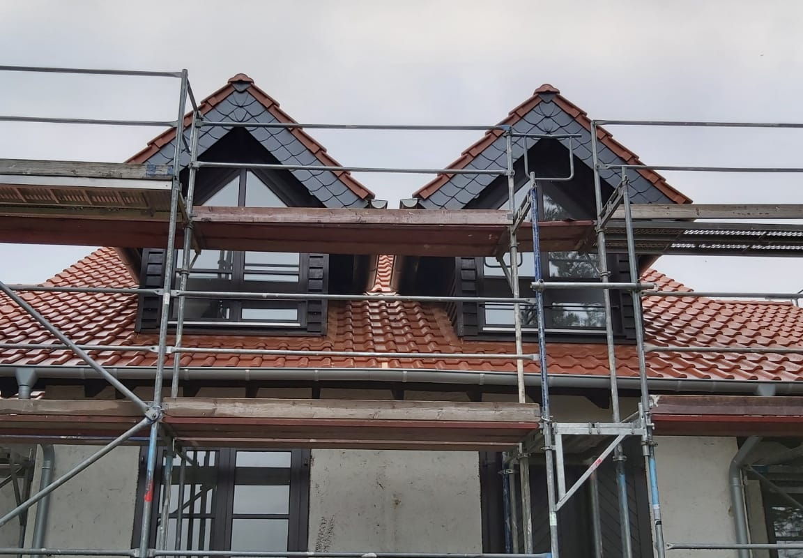 Stirnbretter an zwei Ausbauten mit zwei Reihen Naturschiefer, welches schön im Kontrast zu den roten Dachziegeln steht.