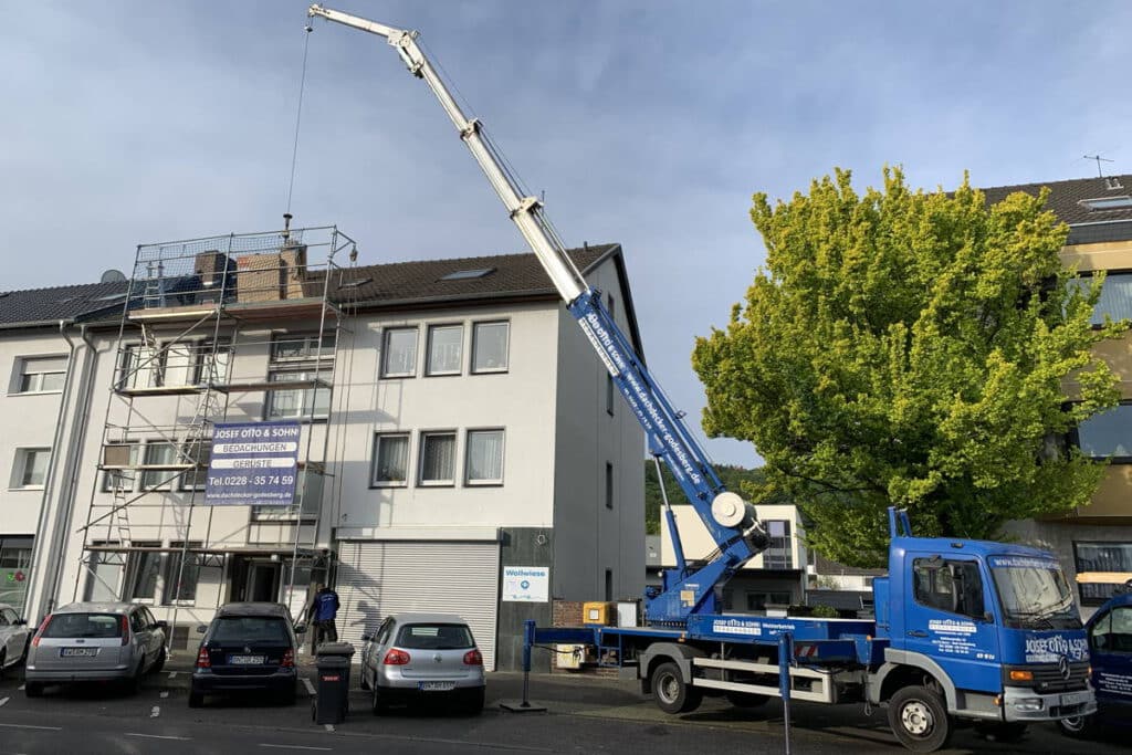 Eingerüstetes Mehrfamilienhaus mit einem dunkelblauen Kran der Firma Josef Otto und Sohn Dachdecker und Bauklempner davor.
