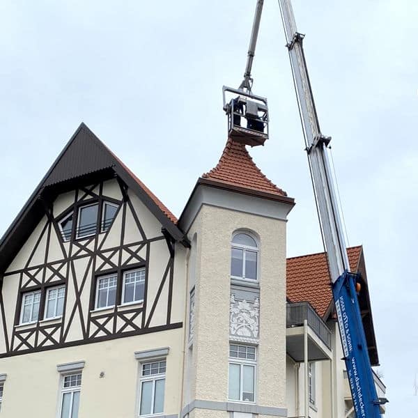 Reparaturarbeiten an der Spitze eines alten Gründerzeithauses mit einem Kran mit Personenkorb.